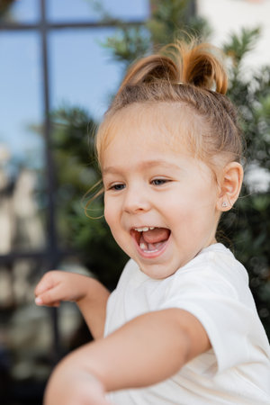 portrait of amazed toddler girl in white t-shirt laughing and looking awayの写真素材