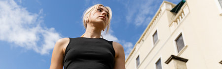 low angle view of blonde woman in tank top standing near building in Miami, banner
