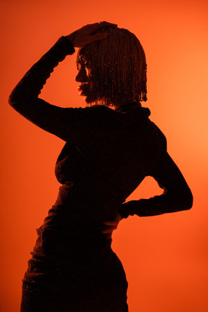 shaded silhouette of sexy glamour woman in black dress and metallic headwear on orange backgroundの写真素材