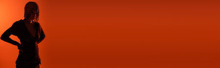 shaded silhouette of sexy woman standing with hands on waist on red and orange background with copy space, bannerの写真素材