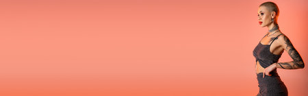 short haired tattooed woman in skirt and crop top standing and looking away on coral pink background, bannerの写真素材