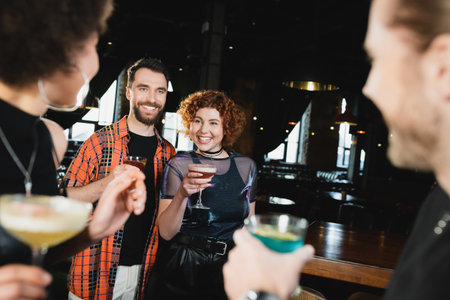 Cheerful people with cocktails meeting blurred interracial friends in barの写真素材