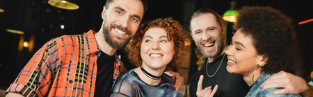 Cheerful multiethnic friends spending time in bar at night, bannerの写真素材