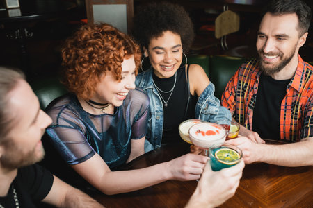 Smiling interracial women holding cocktails near bearded friends in barの写真素材