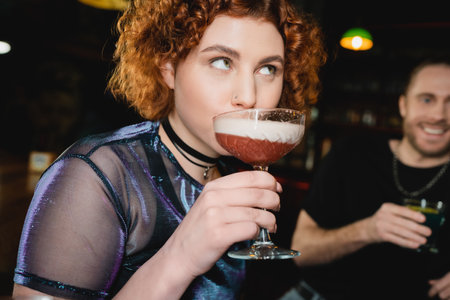 Young red haired woman drinking foam cocktail in barの写真素材