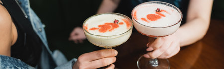 Cropped view of multiethnic girlfriends holding cold foam cocktails in bar in evening, bannerの写真素材