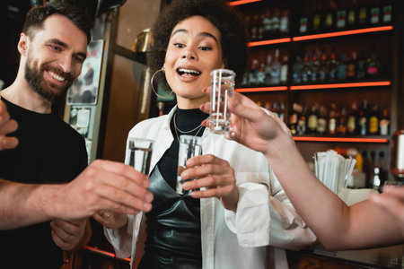 Excited african american woman holding tequila shot with salt near friends in barの写真素材