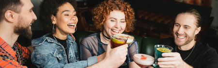 Positive multiethnic people holding different cocktails while clinking in bar, bannerの写真素材