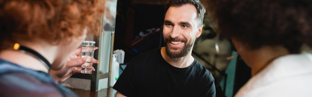 Smiling man looking at blurred interracial friends with tequila in bar, bannerの写真素材