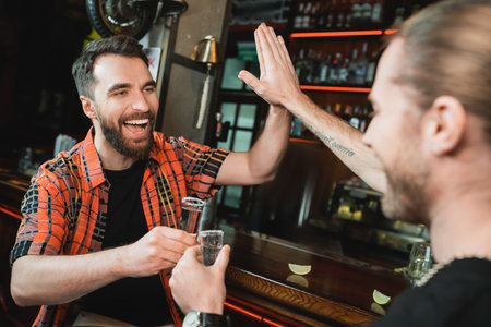 Cheerful bearded men giving high five and holding tequila glasses in barの写真素材