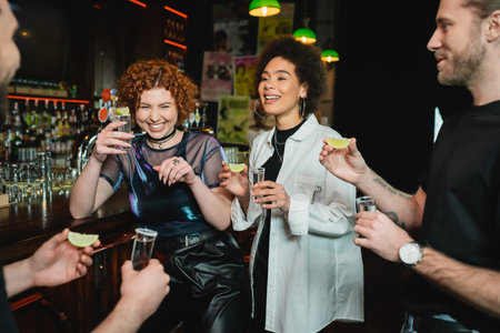 Cheerful multiethnic people having fun and holding tequila shots in barの写真素材