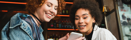 Positive interracial young women using cellphone in bar, bannerの写真素材