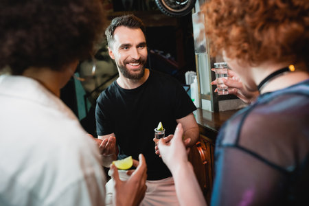 Smiling bearded man talking to blurred interracial friends with tequila in barの写真素材