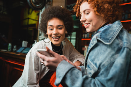 Redhead woman using smartphone with african american friend in barの写真素材
