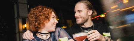Smiling bearded man hugging redhead friend with cocktail in bar, bannerの写真素材