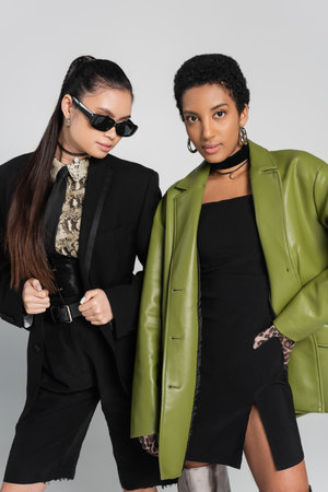 Trendy asian and african american women posing isolated on grey