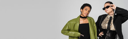 Stylish interracial girlfriends posing isolated on grey with copy space, bannerの写真素材