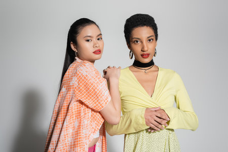 Stylish young multiethnic girlfriends looking at camera on grey backgroundの写真素材