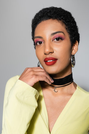 Portrait of short haired african american model with colorful makeup looking at camera on grey backgroundの写真素材