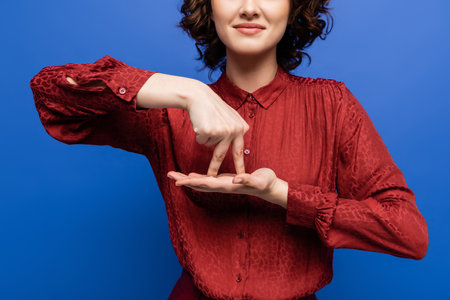 partial view of positive teacher showing gesture meaning stand on sign language isolated on blue