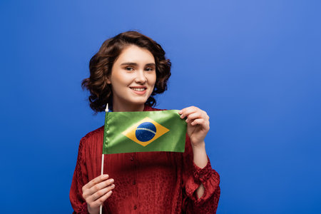 happy language teacher smiling while holding flag of Brazil isolated on blueの写真素材