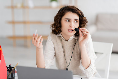 young language teacher in headset holding pen and looking away while working near laptop at homeの写真素材