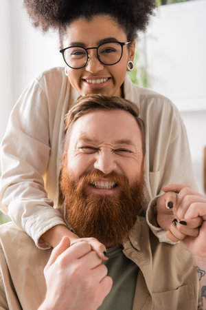 Portrait of positive african american woman holding hands of bearded boyfriend at homeの写真素材