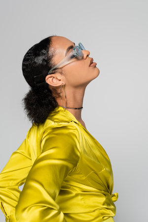 side view of african american model in blue sunglasses and stylish clothes posing isolated on greyの写真素材
