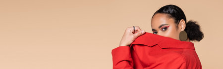 portrait of brunette african american model in bright red blazer covering face while posing isolated...