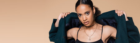 young african american model in crop top wearing dark blue oversized blazer isolated on beige, bannerの写真素材