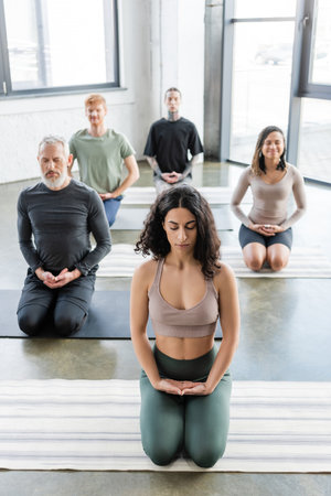 Middle eastern woman meditating in Thunderbolt pose on mat in yoga classの写真素材