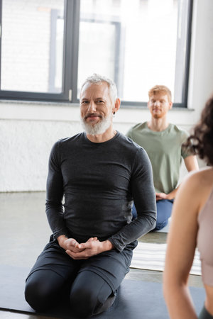 Smiling middle aged man looking at camera while practicing yoga in Thunderbolt asana in studioの写真素材