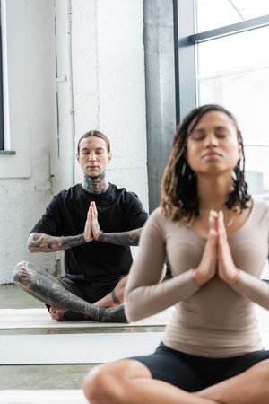 Young tattooed man meditating and doing anjali mudra in yoga classの写真素材