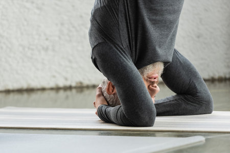 Mature man doing Supported Headstand asana on mat in yoga studioの写真素材