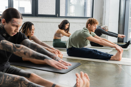 Young african american woman stretching on mat near people in yoga studioの写真素材
