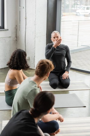 Mature coach showing nostril breathing to blurred group in yoga studioの写真素材