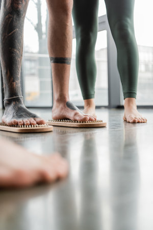 cropped view of tattooed man standing with bare feet on nail board near woman in yoga studioの写真素材