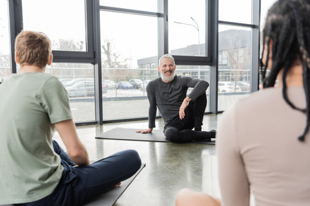 Positive coach looking at blurred multiethnic people in yoga studioの写真素材