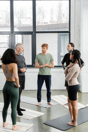 Interracial people looking at mature coach while standing on mats in yoga classの写真素材