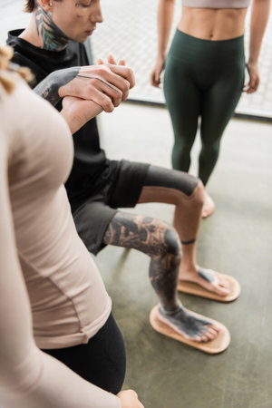 tattooed man sitting on chair while putting bare feet on sadhu board near women in yoga studioの写真素材