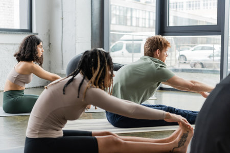 Side view of young interracial people stretching while doing seated forward bend asana in yoga studioの写真素材