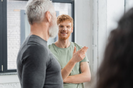 Smiling redhead man talking to blurred coach in yoga classの写真素材