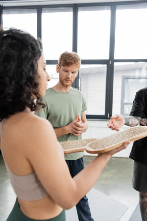 Redhead man standing near middle eastern woman with sadhu board in yoga classの写真素材