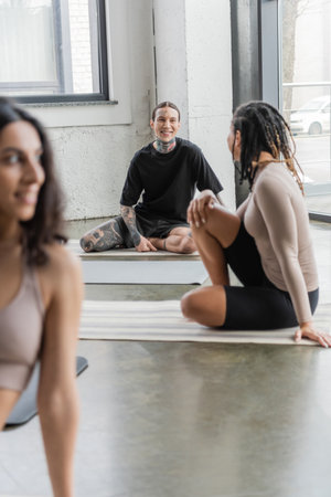 Smiling interracial people talking while sitting on mats in yoga classの写真素材