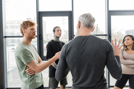 Redhead man talking to blurred mature coach in yoga studioの写真素材