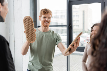 Positive man holding sadhu board near blurred multiethnic group in yoga studioの写真素材