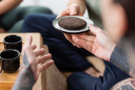 cropped view of tattooed man taking plate with compressed and fermented puer teaの写真素材