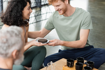 happy middle eastern woman giving compressed puer tea to smiling redhead man in yoga studioの写真素材