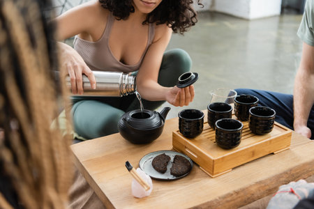cropped view of woman pouring hot water from flask while brewing pu-erh tea near people in yoga studioの写真素材