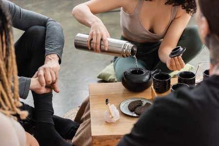 cropped view of woman pouring hot water from flask while brewing puer tea near people in yoga studioの写真素材